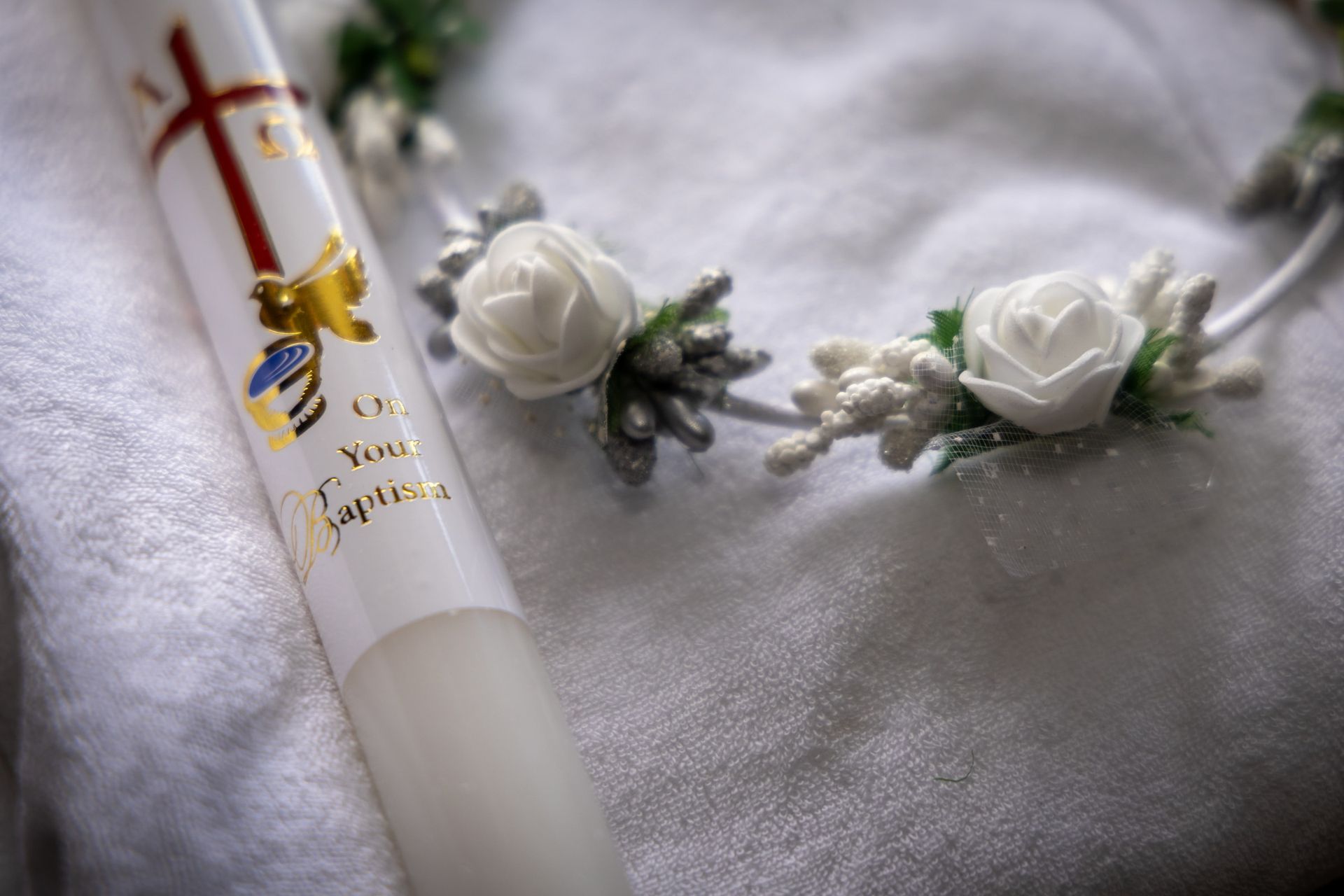 A decorated baptism candle and white floral accessories resting on soft fabric