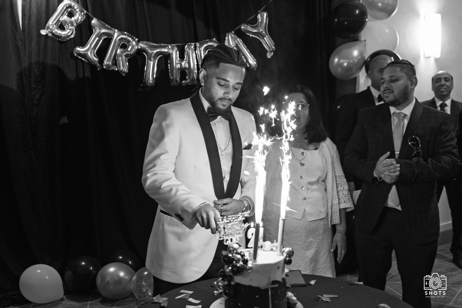 Black-and-white photograph of friends gathered around a birthday cake with sparklers