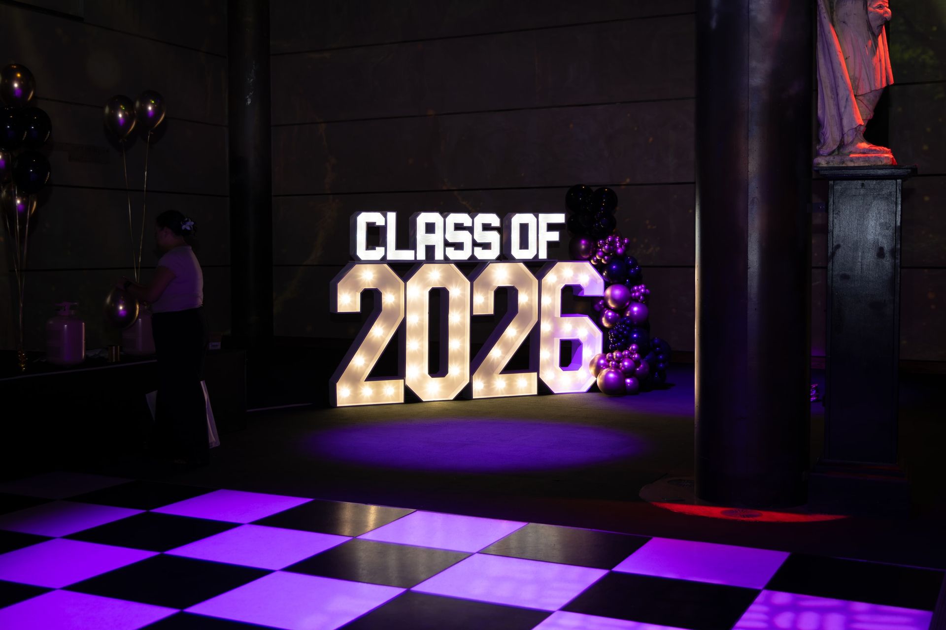 An illuminated Class of 2026 sign beside a purple-lit dance floor