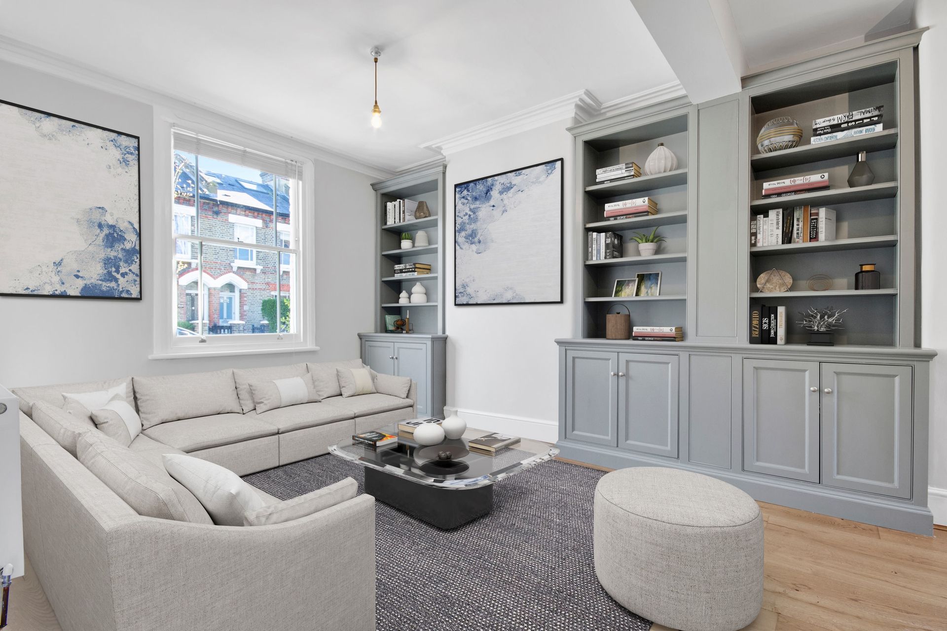 A bright living room with pale sofas, grey built-in shelves and a large window