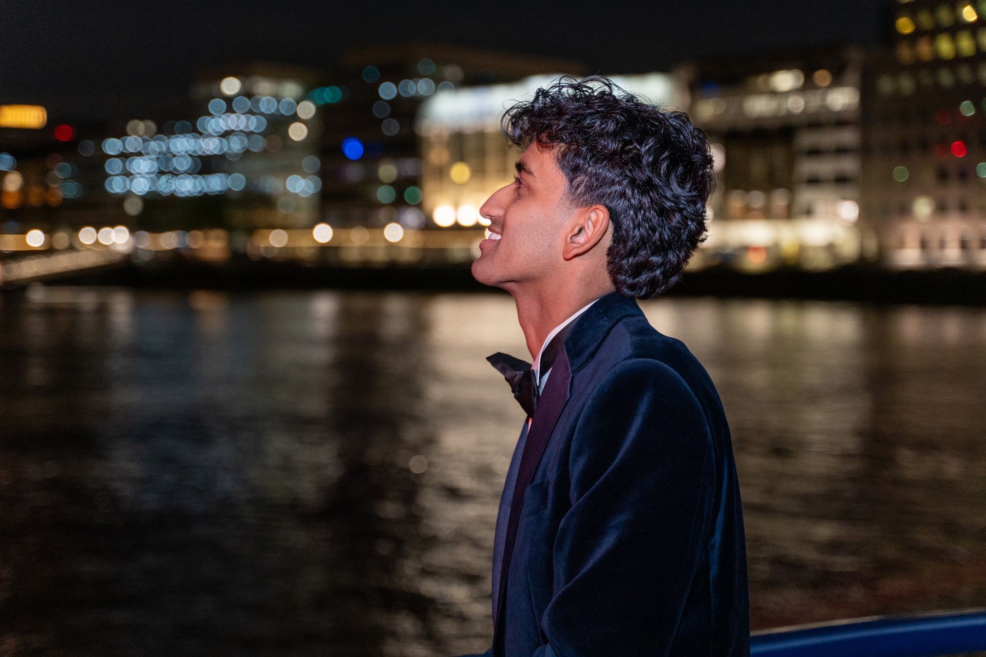 A guest in evening dress looking across the river with London lights behind him